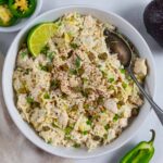 White bowl of artichoke jalapeño chicken salad with a spoon and lime wedge.