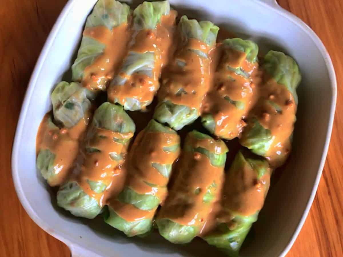 Cabbage rolls before baking, in baking pan with peanut sauce poured on top.