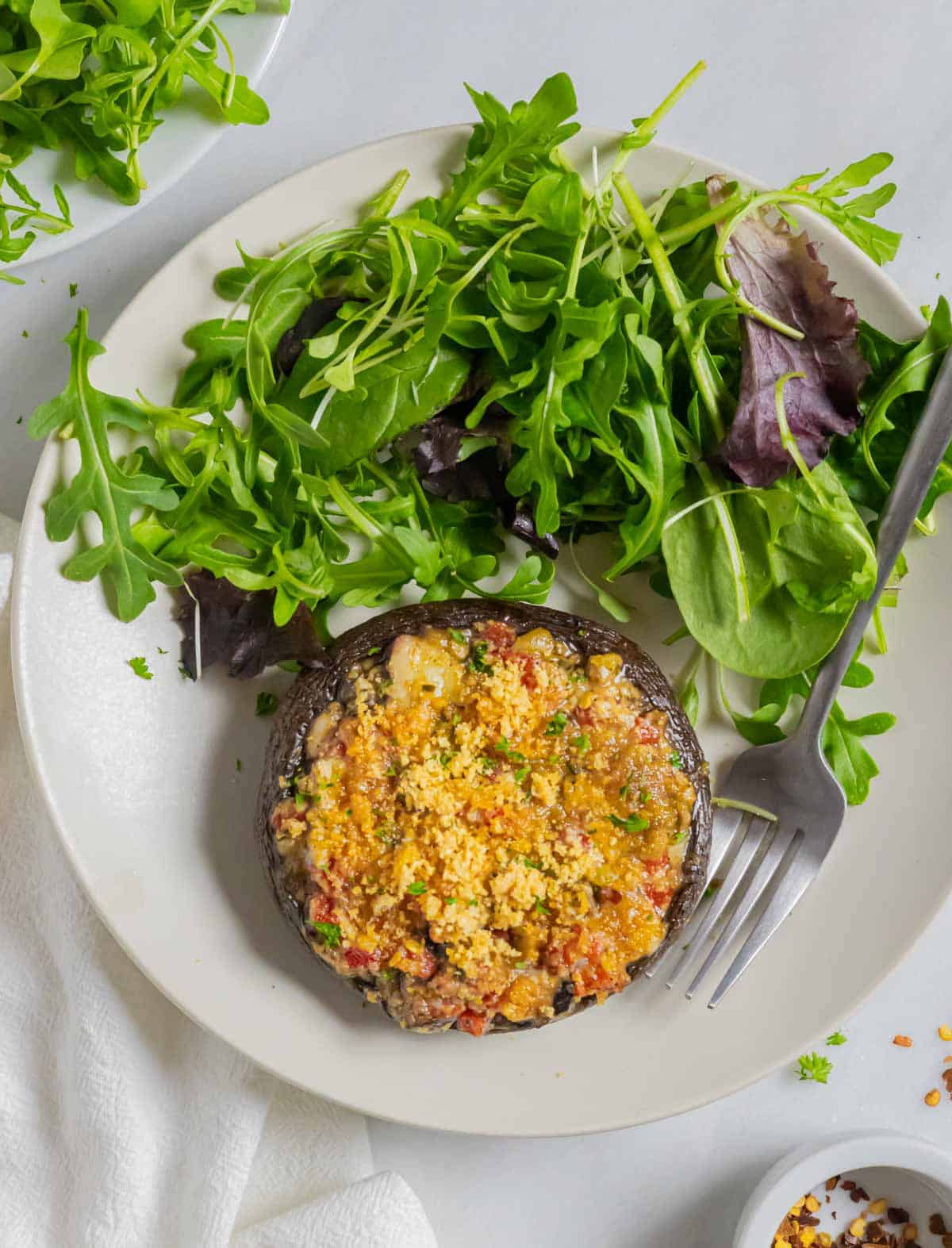 Stuffed portobello mushroom on a white plate with salad greens and a fork.
