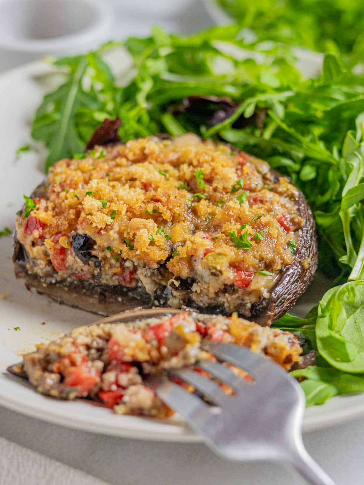 Smoked stuffed portobello on a plate with greens and a slice cut and on a fork.