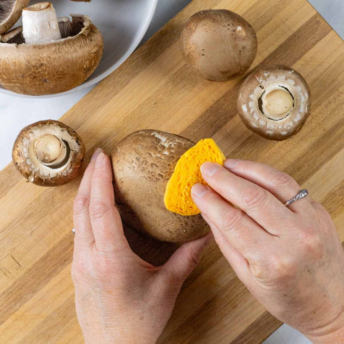 Hands using a sponge to clean the outside of mushrooms.
