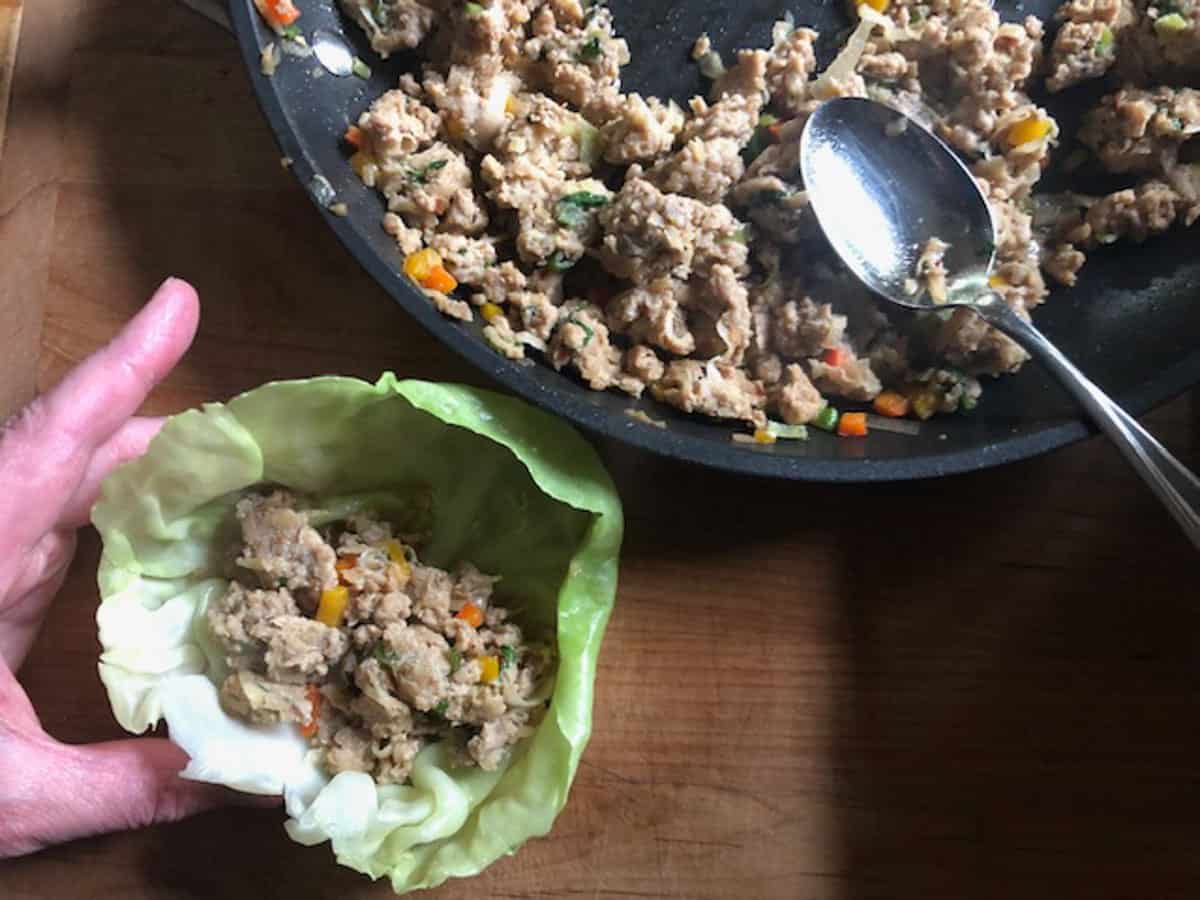 Cabbage leaf with filling and a pan with ground chicken cabbage roll filling with a spoon.