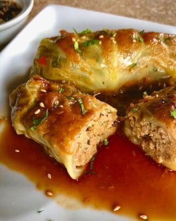 One whole Asian Cabbage Roll and one cut in half on a plate sitting in dipping sauce.