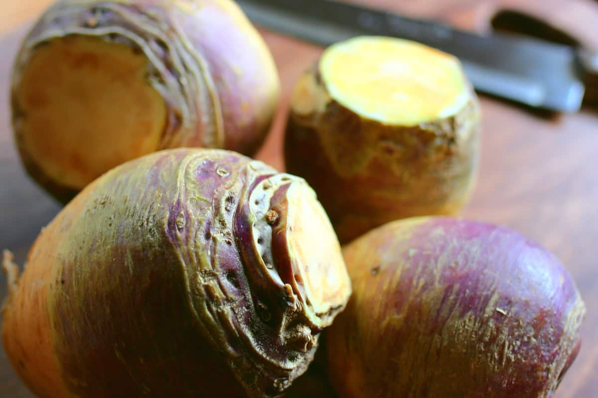 Whole rutabagas on a brown butting board with a knife.