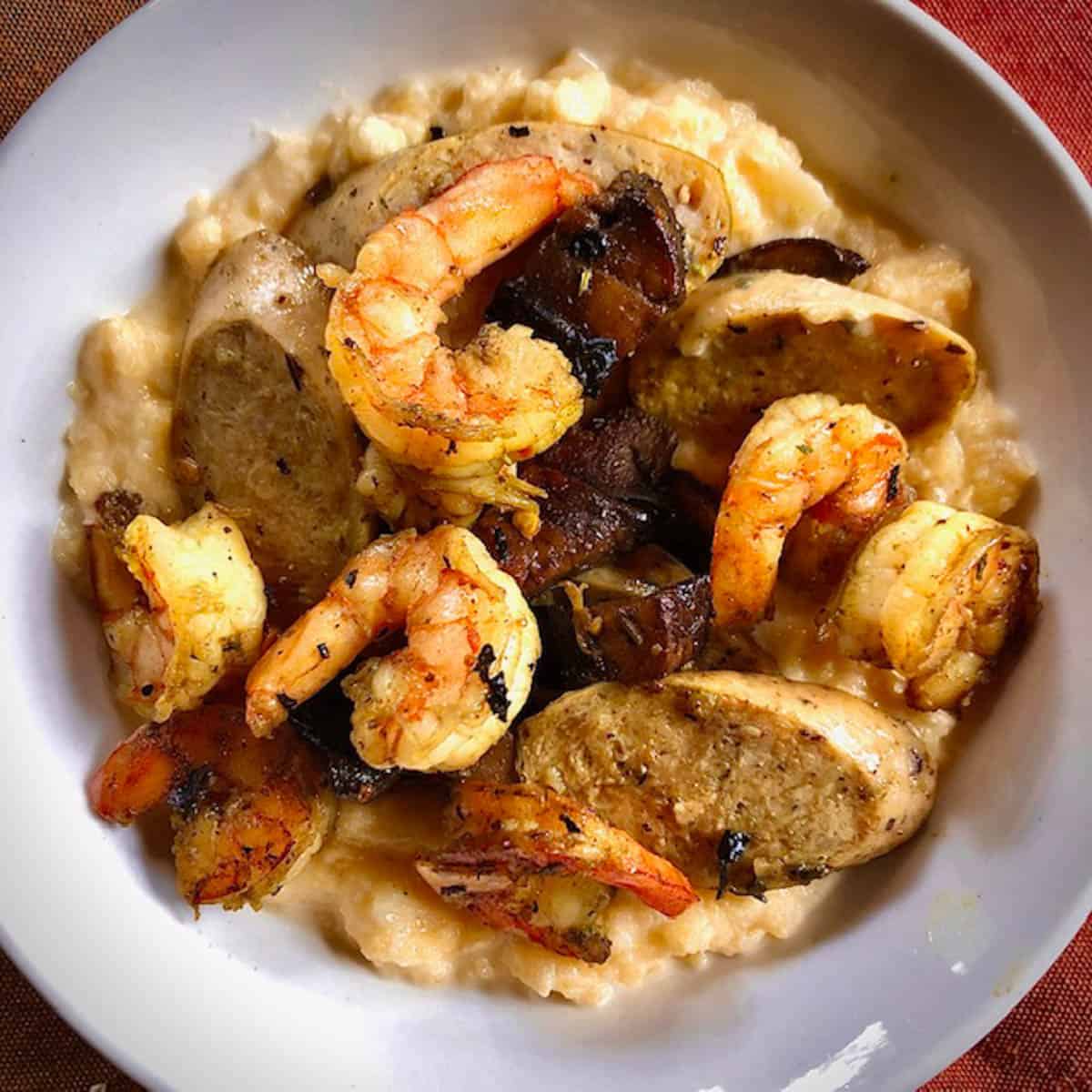 Bowl of sauteed shrimp, and sausage slices on a bed of rutabaga skordalia grits.