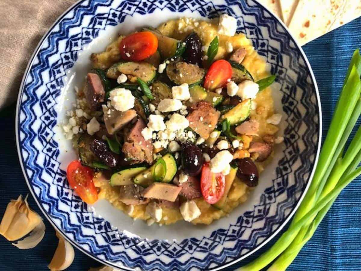 Blue and white bowl of finished stir fry with feta cheese and kalamata olives on skordalia.