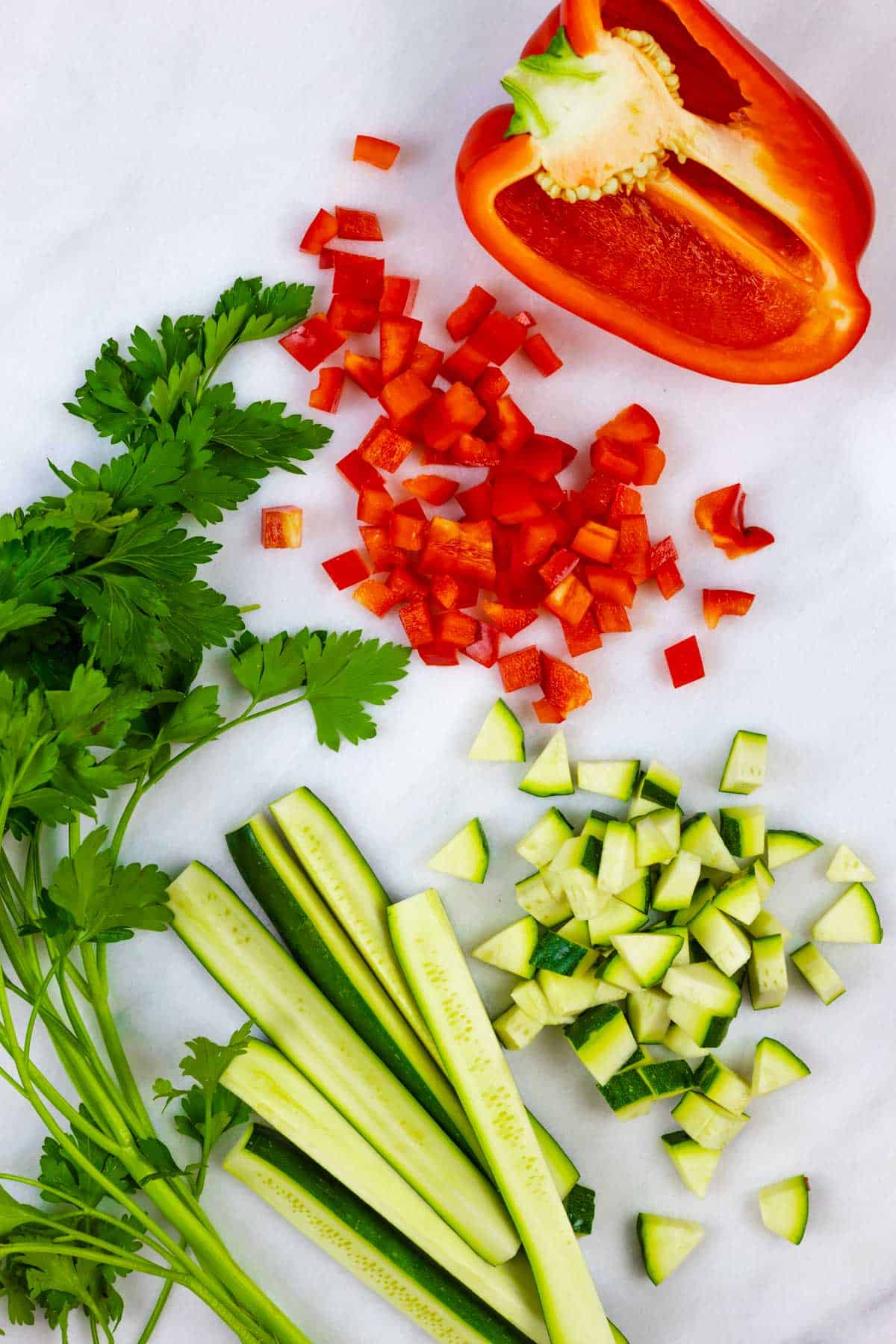 Chopped zucchini and red bell pepper on a light marble board with sprig of cilantro.
