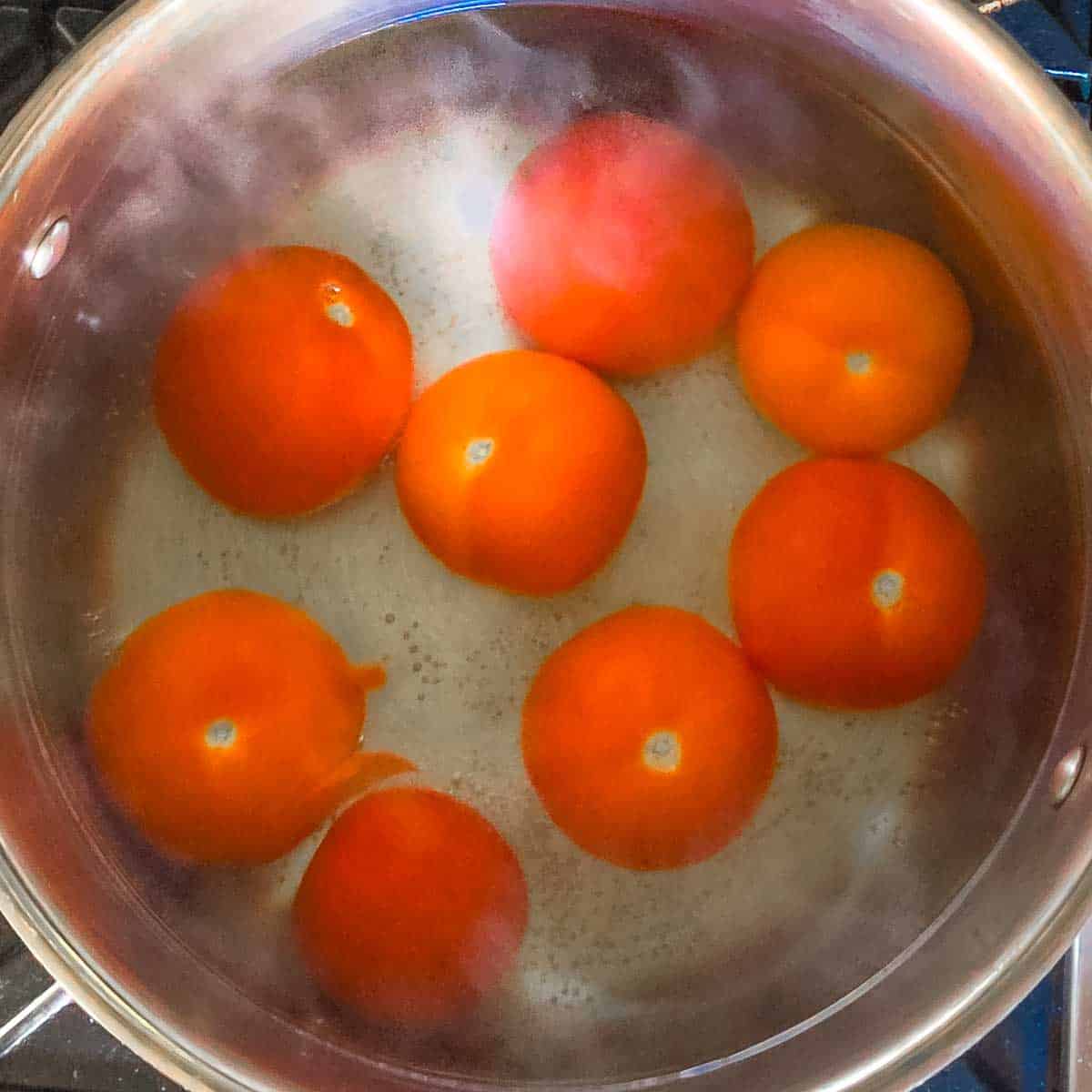 Red tomatoes being blanched and steaming in a large pot of hot water.