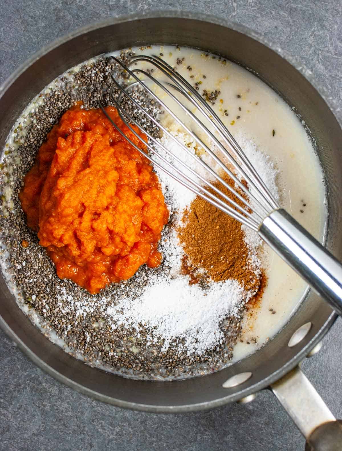 Ingredients in a sauce pan with a whisk not yet mixed together with focus on the pumpkin puree.