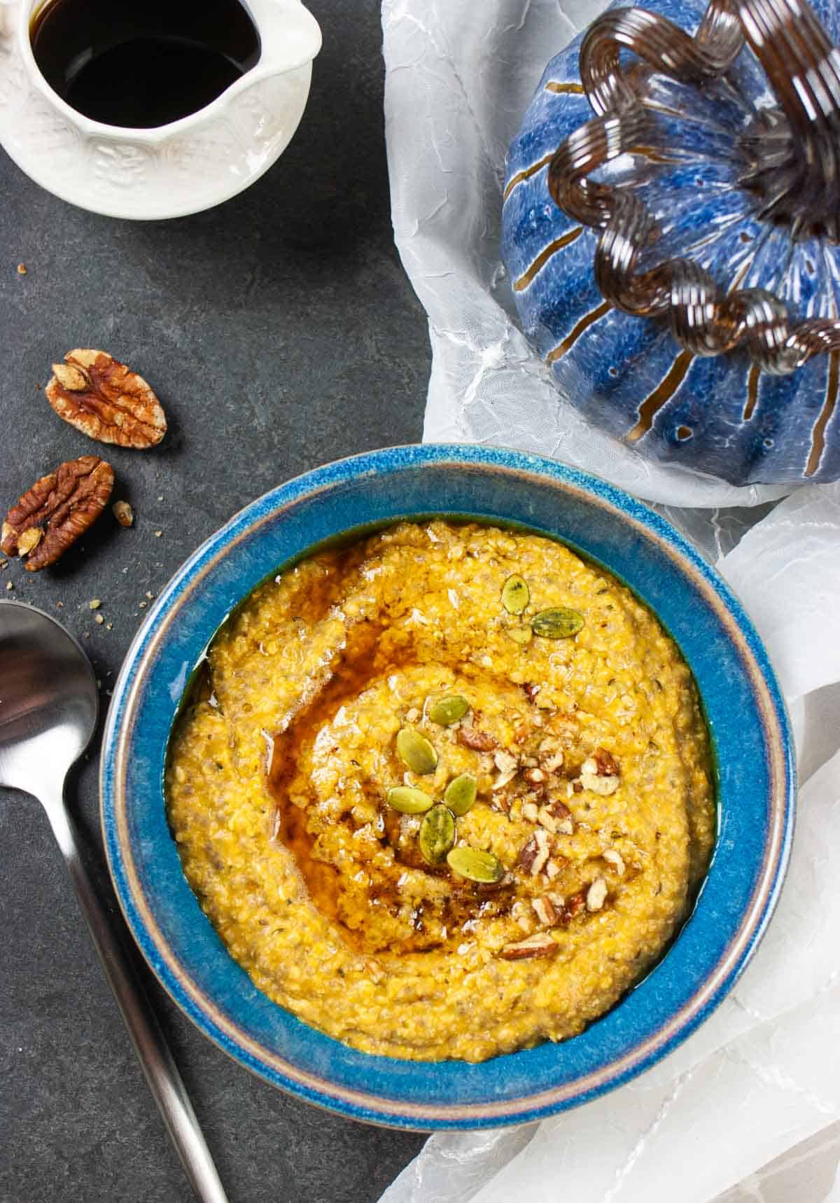 Blue bowl of porrige topped with syrup and nuts with pecans, small bowl of syrup and a blue glass pumpkin on the side.