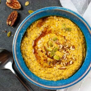 Pumpkin porridge in a blue bowl with a spoon laying next to it and pecan halves.