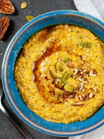 Pumpkin porridge in a blue bowl with a spoon laying next to it and pecan halves.