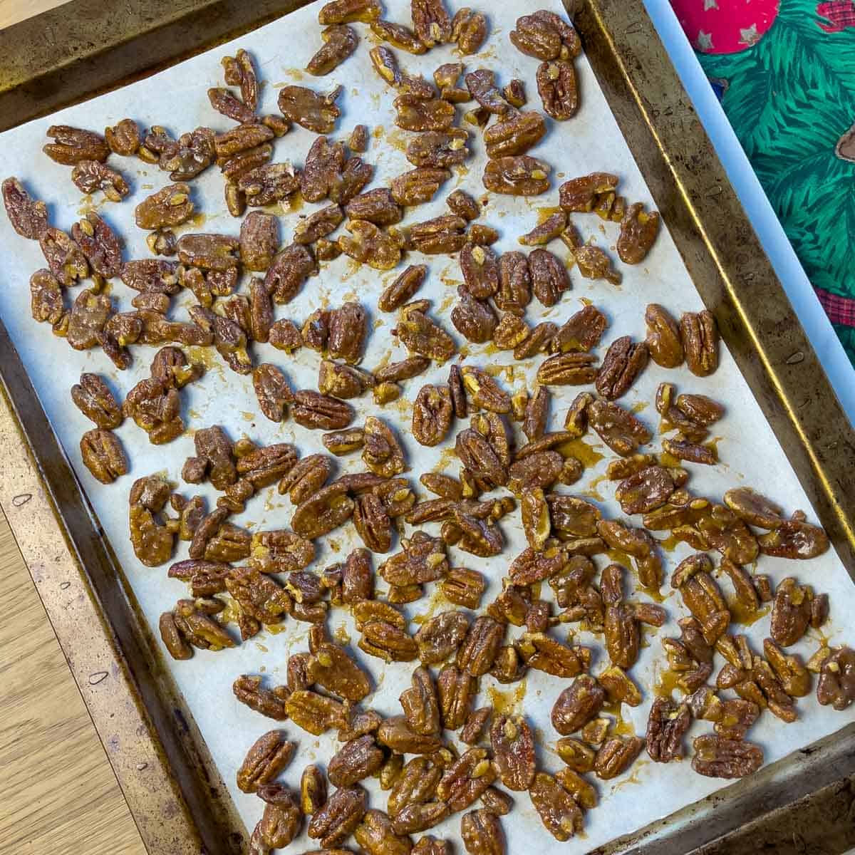 Spice coated pecans spread on a parchment lined baking sheet ready to go into the oven.