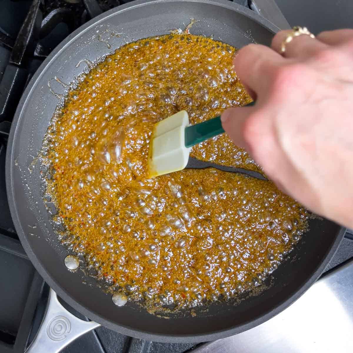 Skillet of butter and spices simmering on the stove while being stirred with a rubber spatula.