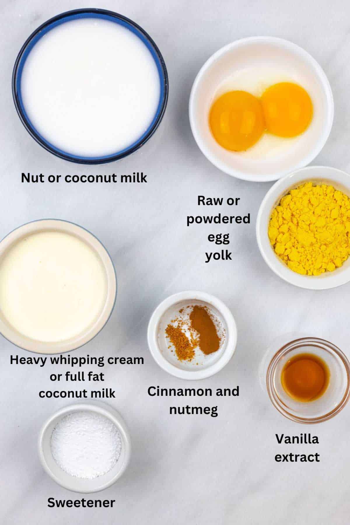 Labeled small bowls of eggnog ingredients on a marbel board, some with substitutes.