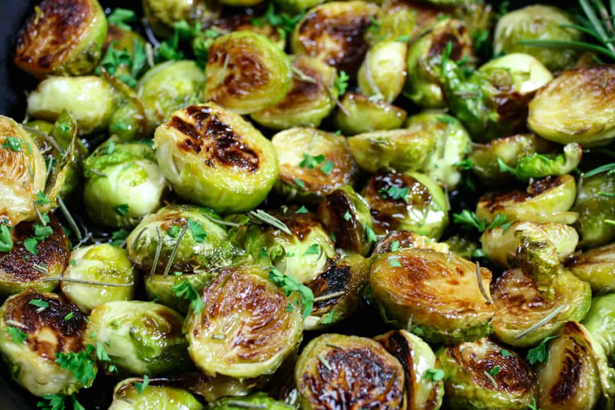 Crispy brussels sprouts close up sprinkled with parsley and rosemary.