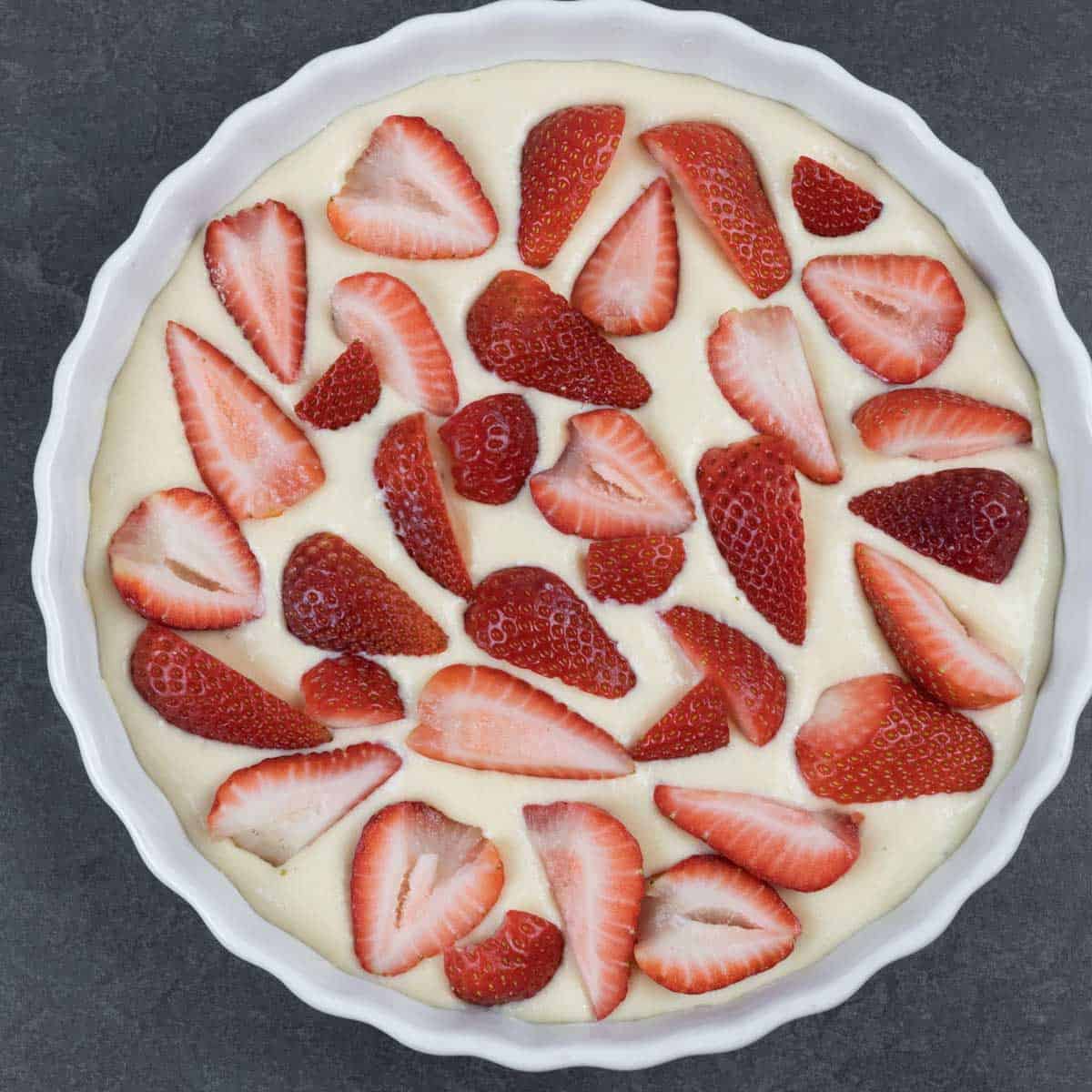 Clafoutis batter in tart dish topped with strawberry quarters ready for the oven.