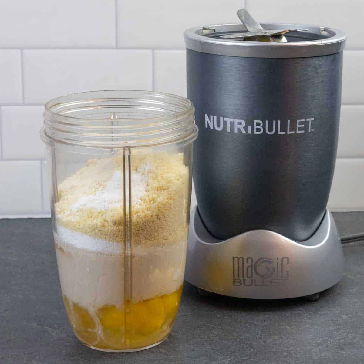 Raw ingredients for clafoutis layered in a blender cup next to a Nutribullet blender.