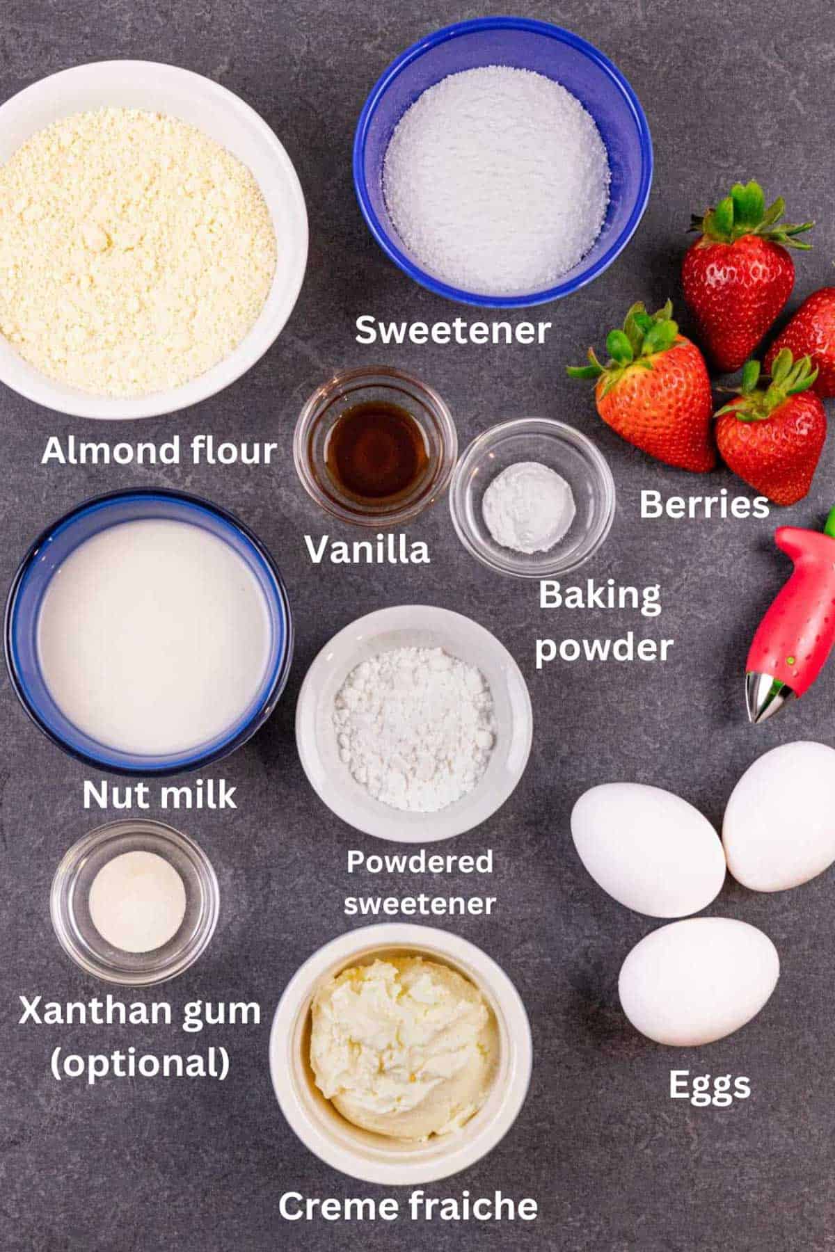 Clafoutis ingredients in small bowls laid out on a grey board with white text labels.
