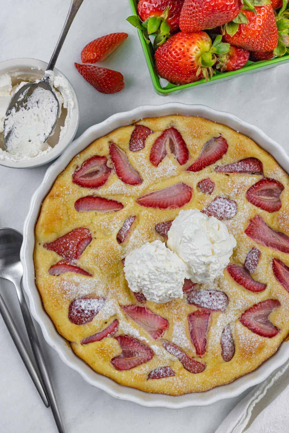 Baked clafoutis with strawberries in tart dish topped with two dollops of keto whipped cream.