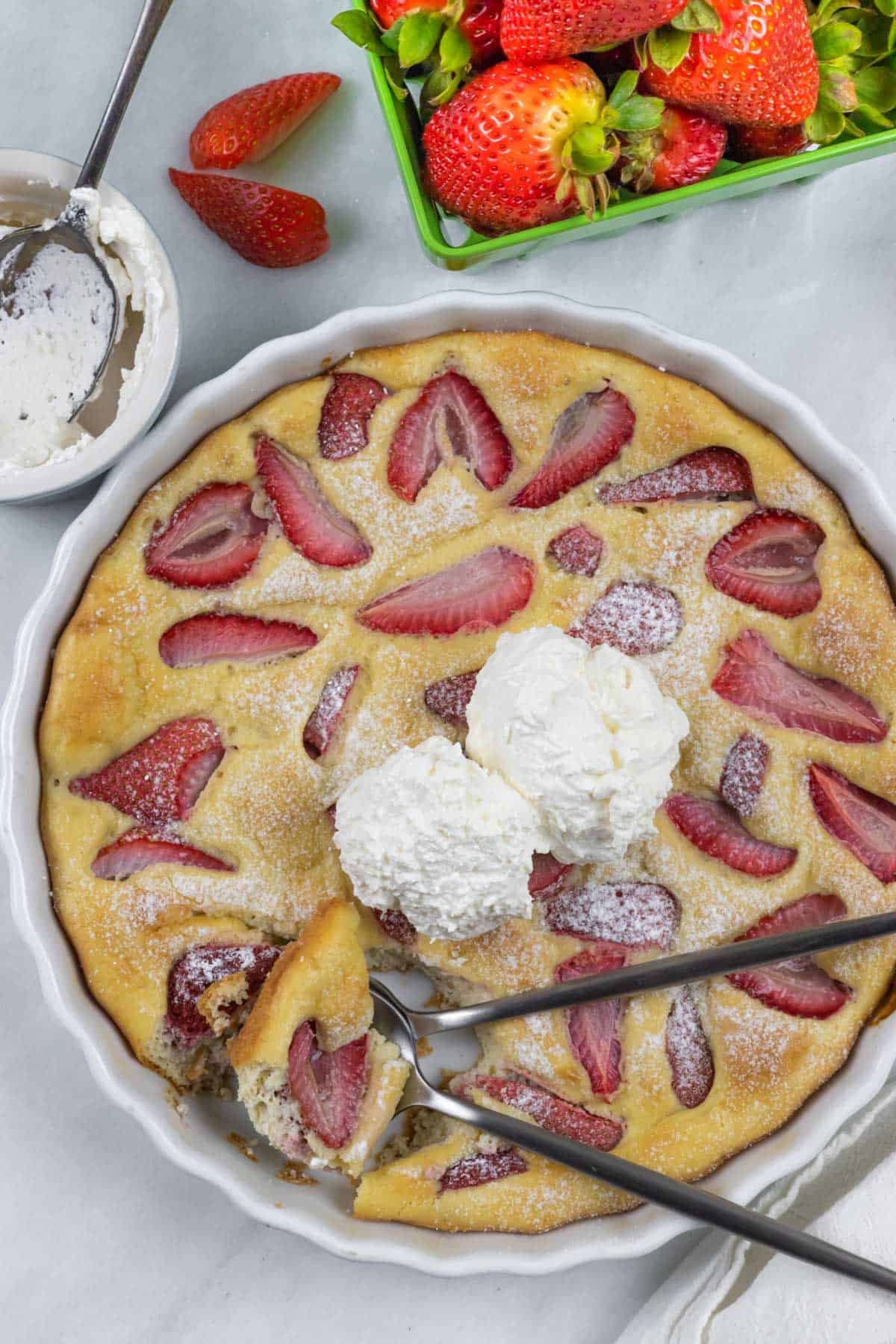 Strawberry clafoutis in pie dish with two overlapping spoons taking a scoop.