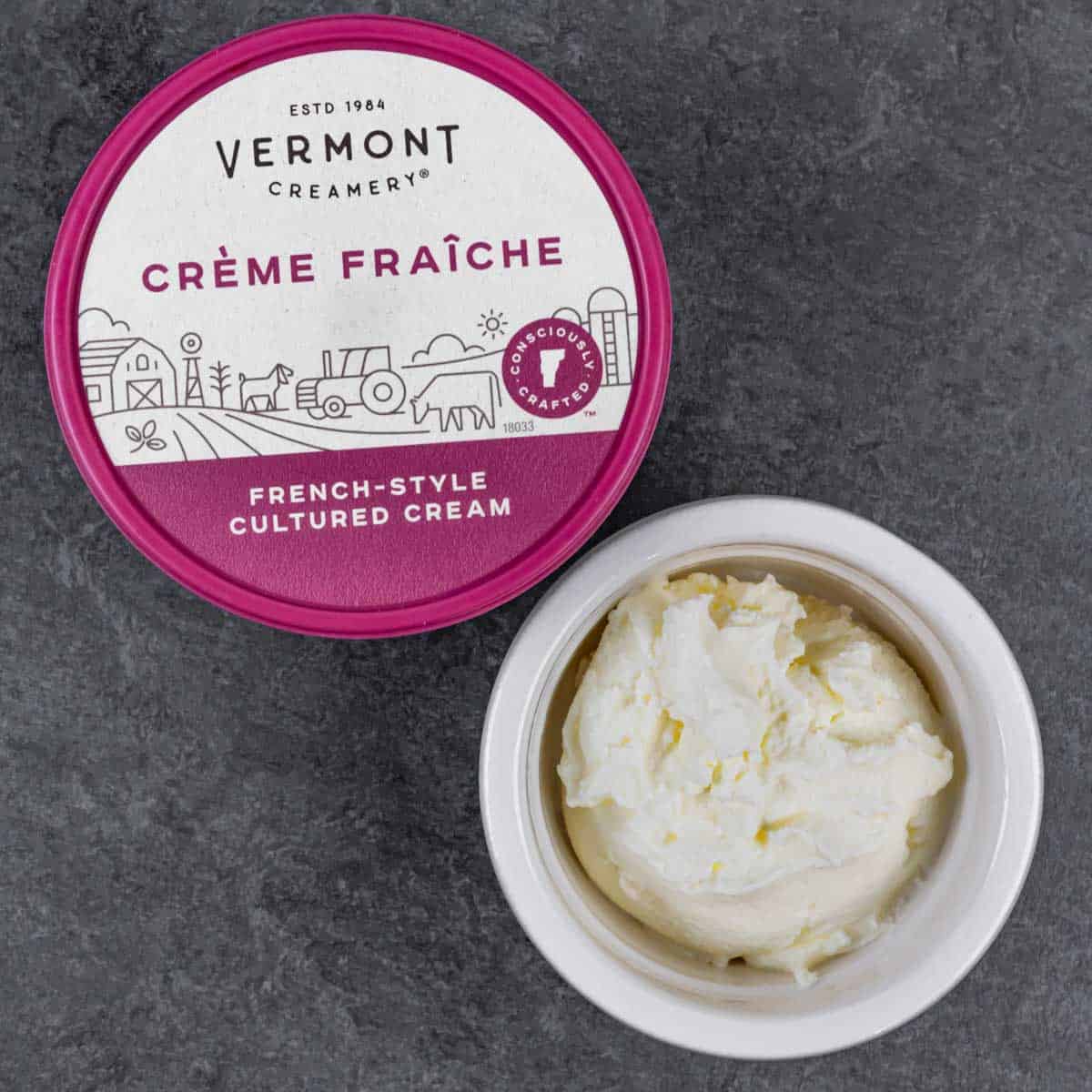 Tub of Vermont Creamery french-style cultured cream with a small ramekin full on the side on a grey board.