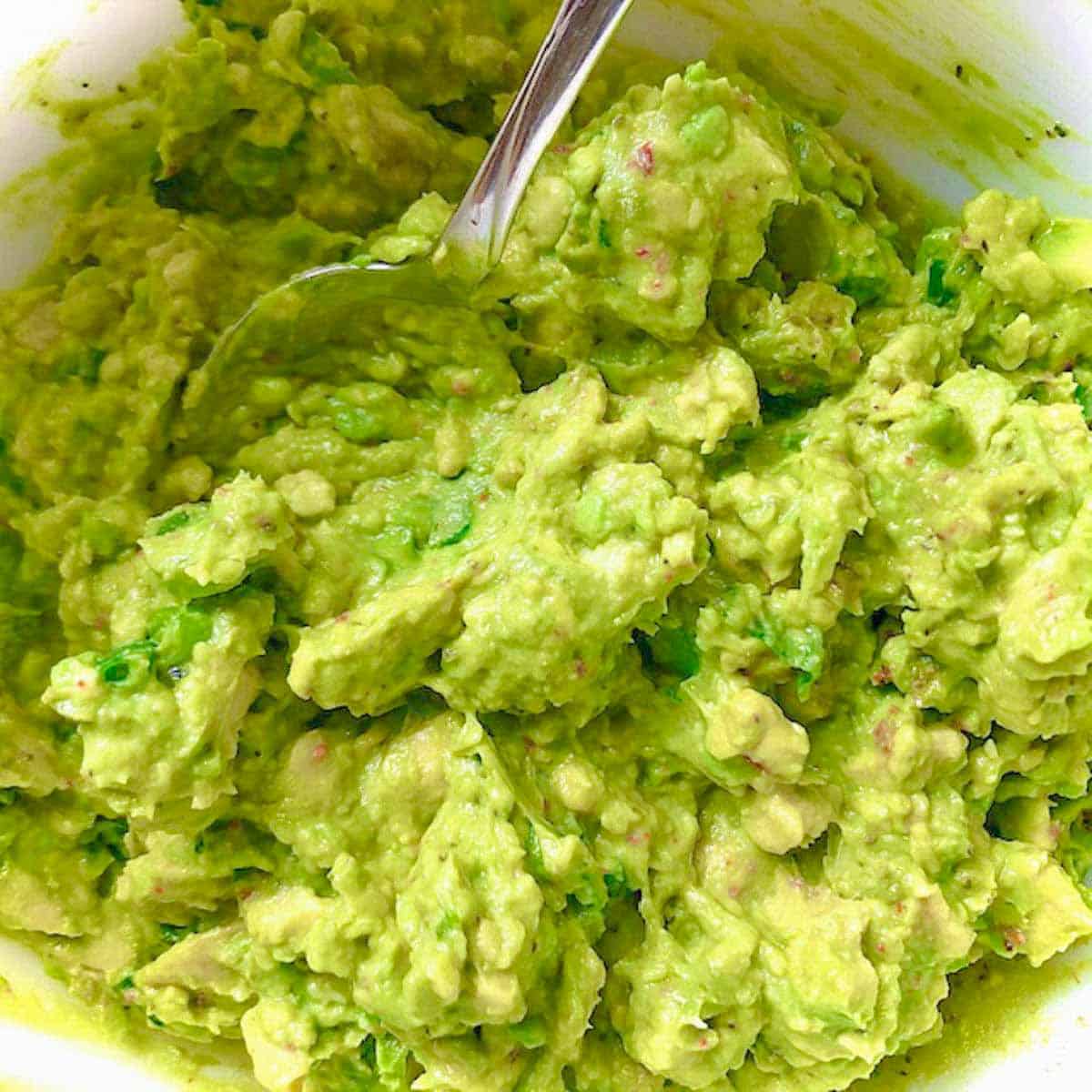Guacamole ingredients mashed together and in a bowl with a spoon.