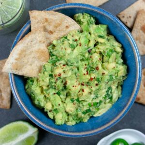 Low-FODMAP guacamole in a blue bowl with chips dipped in it.