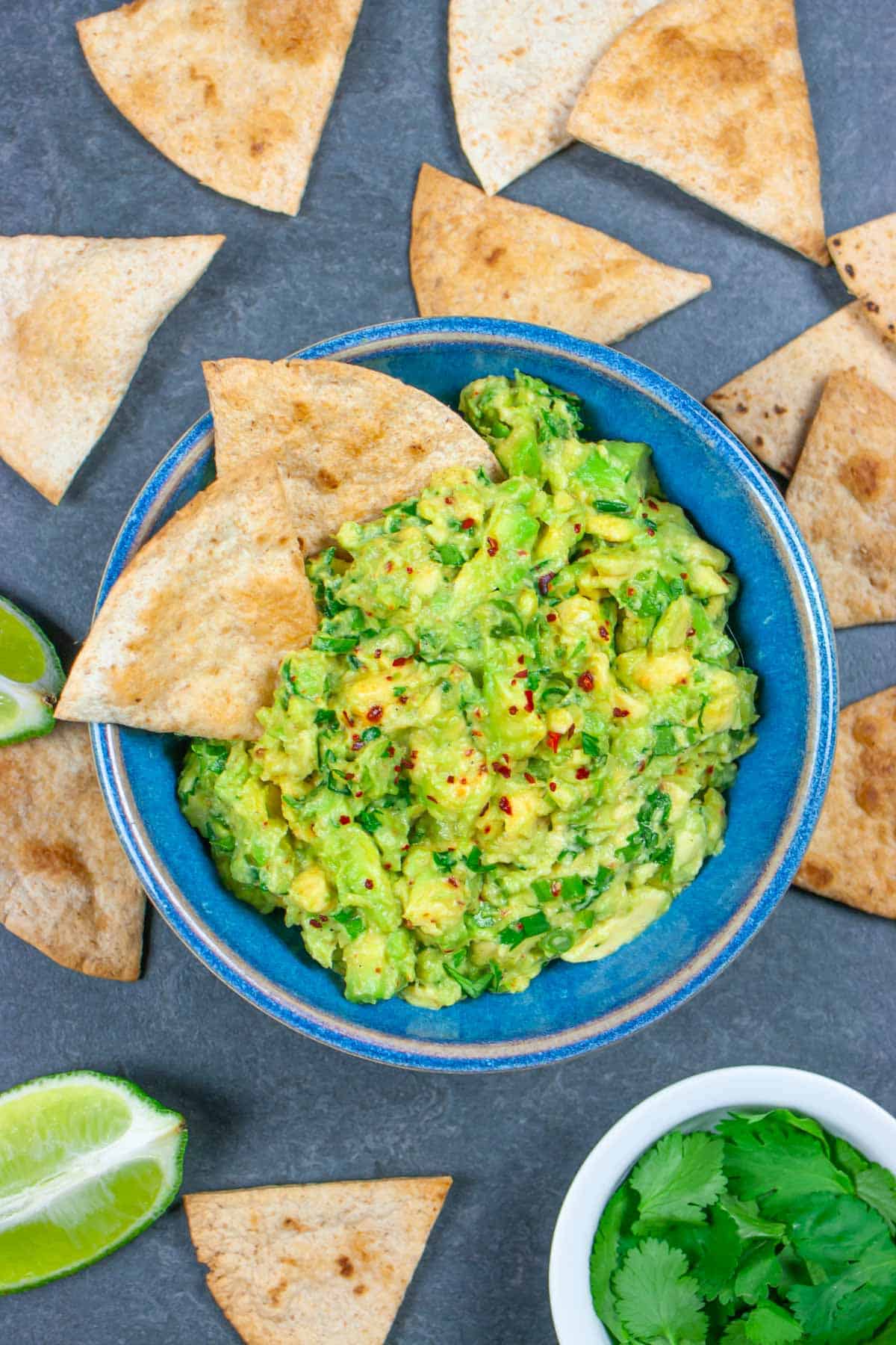 Guacamole dip in a blue bowl with two triangle chips in it, and sprinkled with Aleppo pepper.