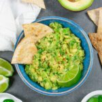 Low-fodmap guacamole in a blue bowl with chips and limes on the side.
