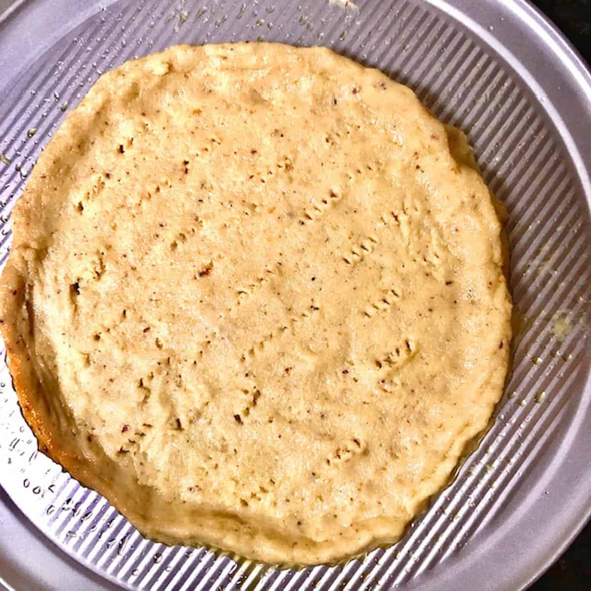 Keto fathead dough pizza crust rolled out on a pizza pan and fork poked ready to bake.