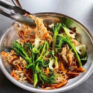 Lo mein being served out of a steel skillet with tongs.