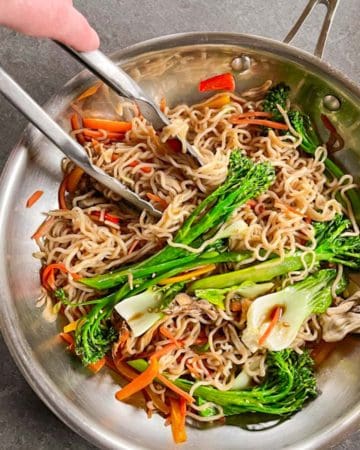 Finished keto Lo Mein recipe in a stainless steel skillet with steel tongs reaching in.