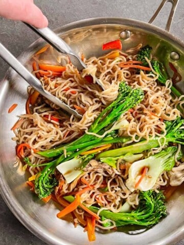 Finished keto Lo Mein recipe in a stainless steel skillet with steel tongs reaching in.