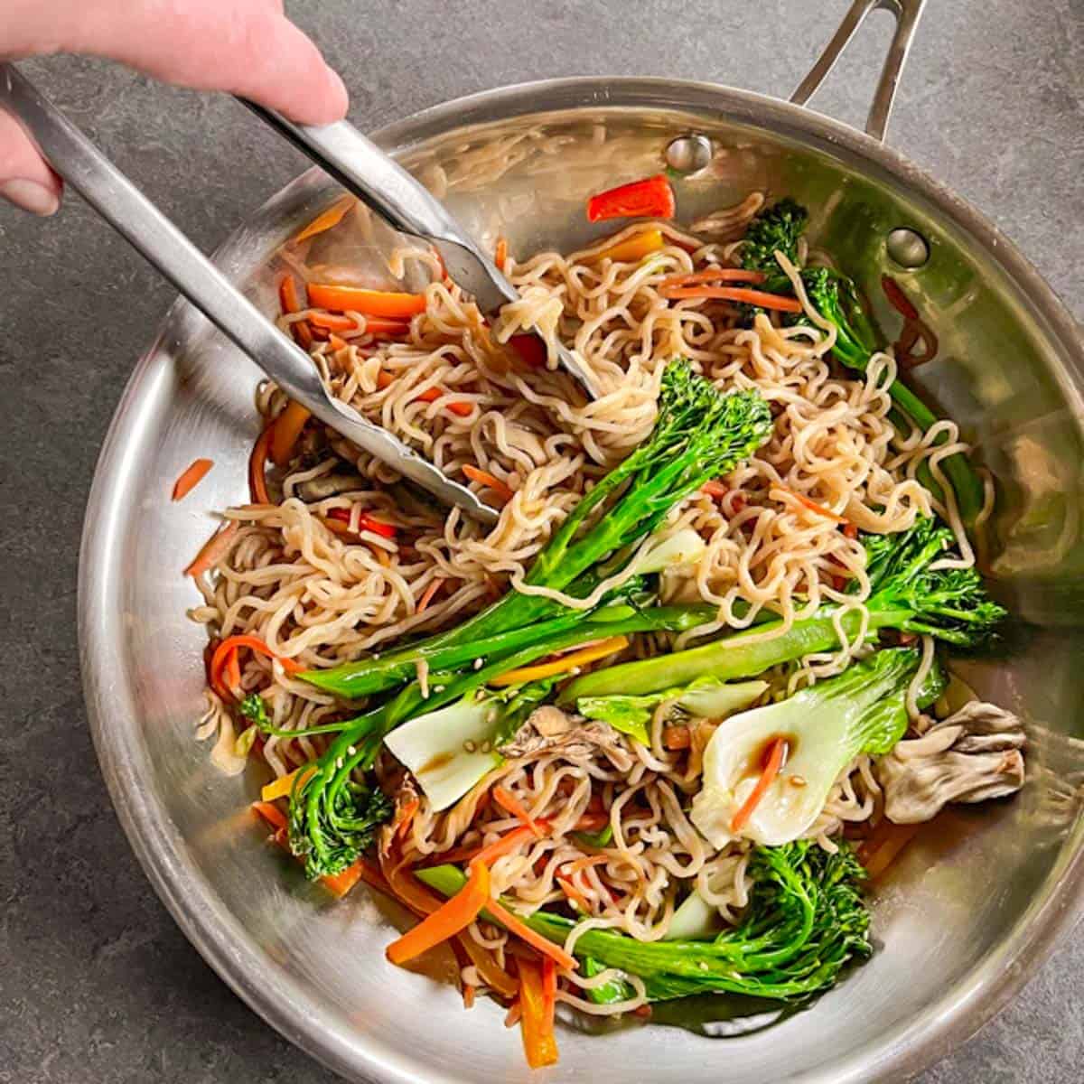 Finished keto Lo Mein recipe in a stainless steel skillet with steel tongs reaching in.