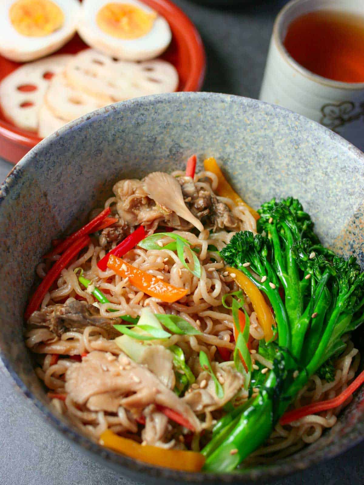 Lo Mein served in a bowl with a side of hard boiled egg halves and tea in a cup.