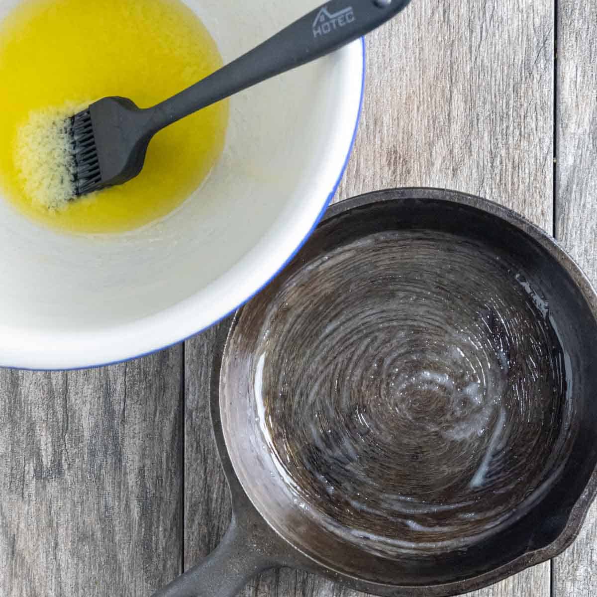Melted butter in a bowl with a basting brush next to a buttered small cast iron skillet.