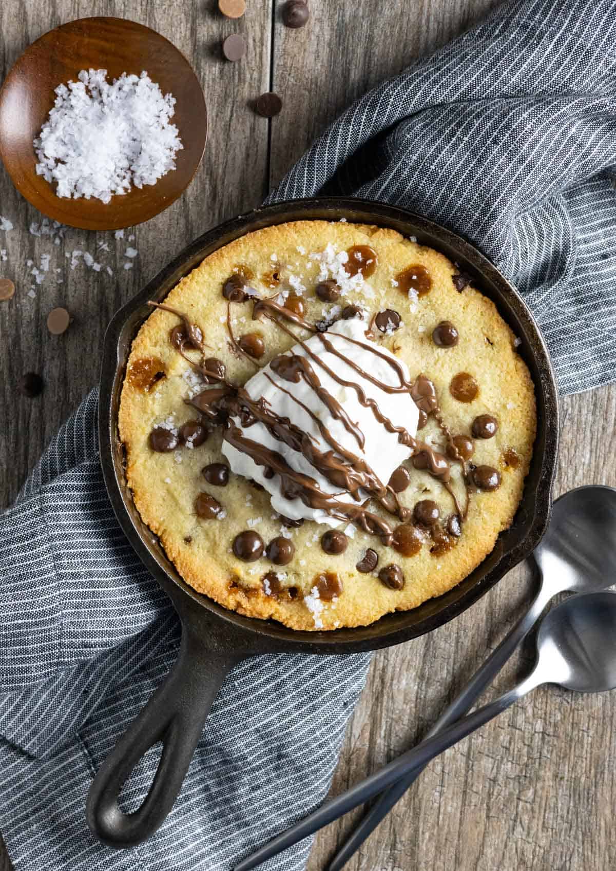 Cast iron mini skillet cookie topped with chips, whipped cream and a drizzle of melted chocolate.