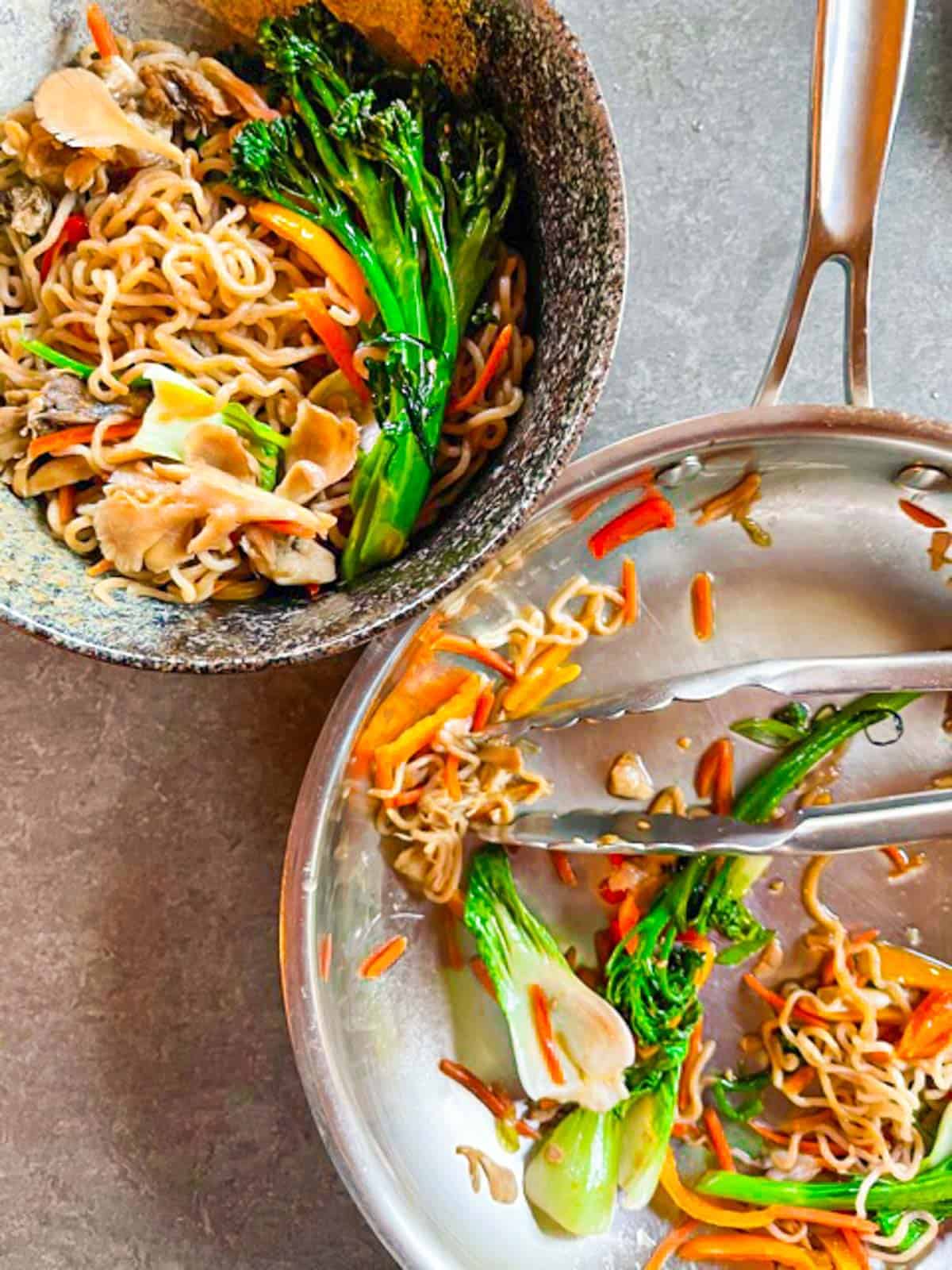 Lo mein being served from a pan into a bowl with tongs.