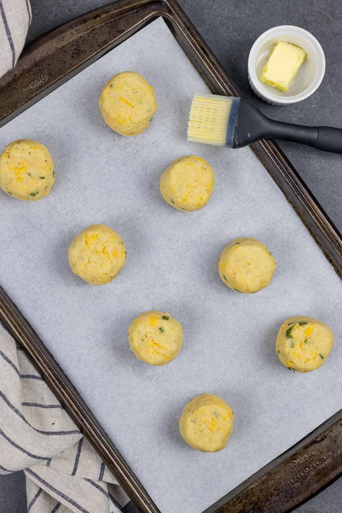 Parchment lined baking sheet with rolled biscuit dough balls with captioned instruction.