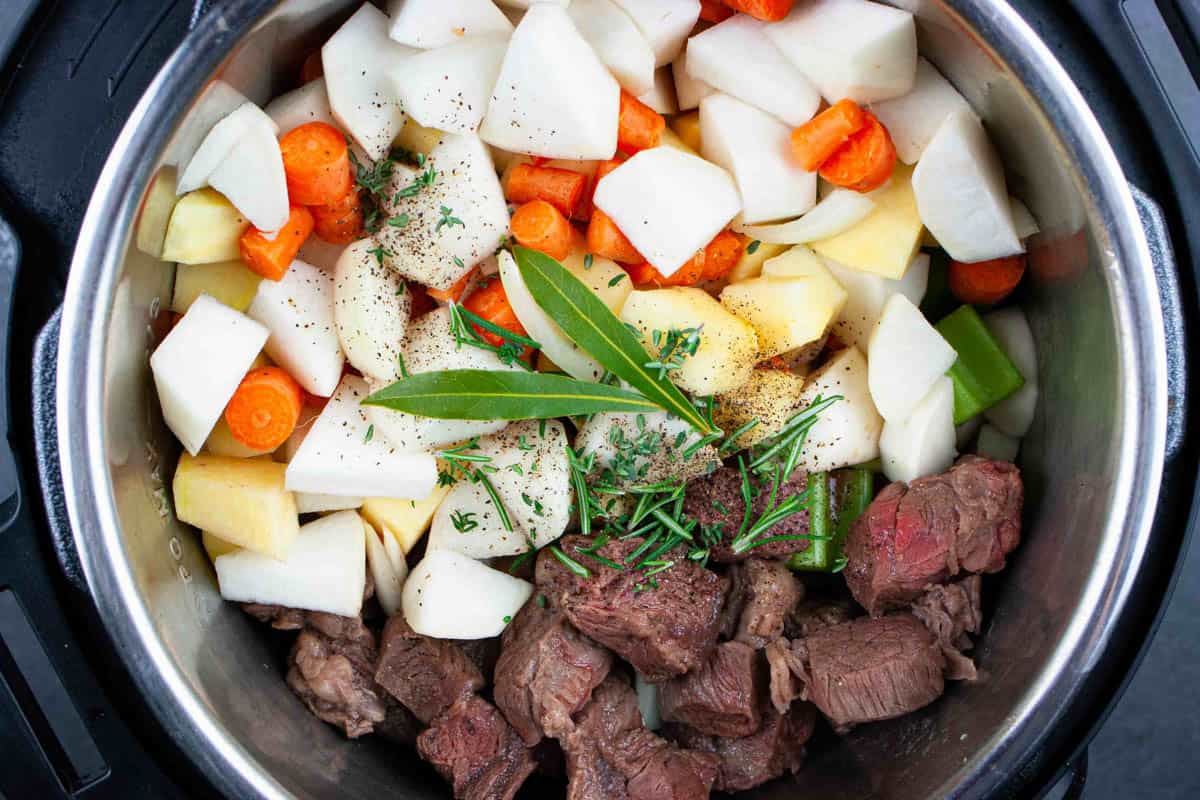 Beef stew ingredients in the instant pot topped with two bay leaves.