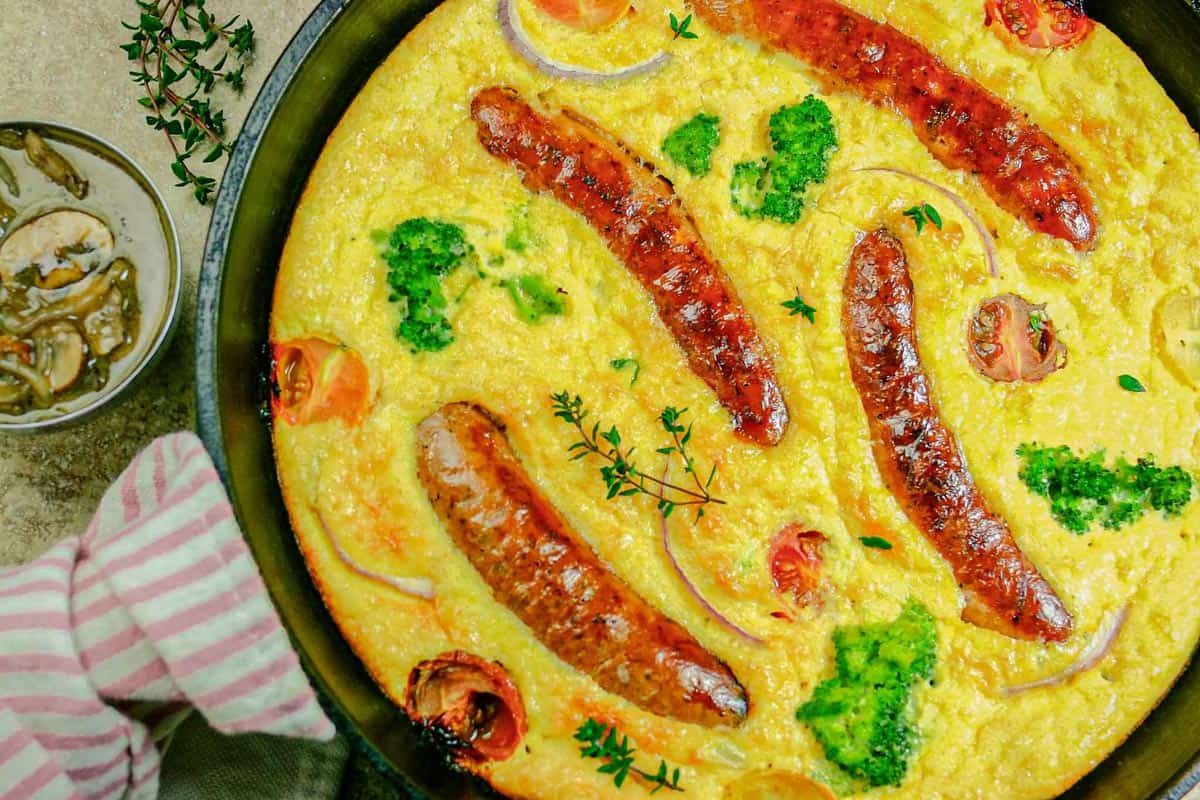 Toad in the hole in a hot cast iron skillet with small side bowl of gravy.