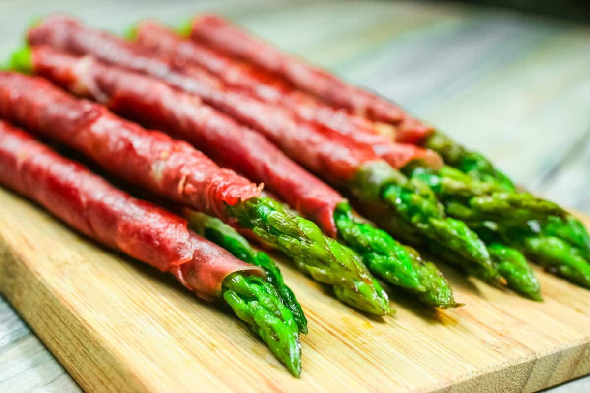 Small group of Asparagus wrapped in crispy prosciutto on a bamboo cutting board focused on the Asparagus tips.