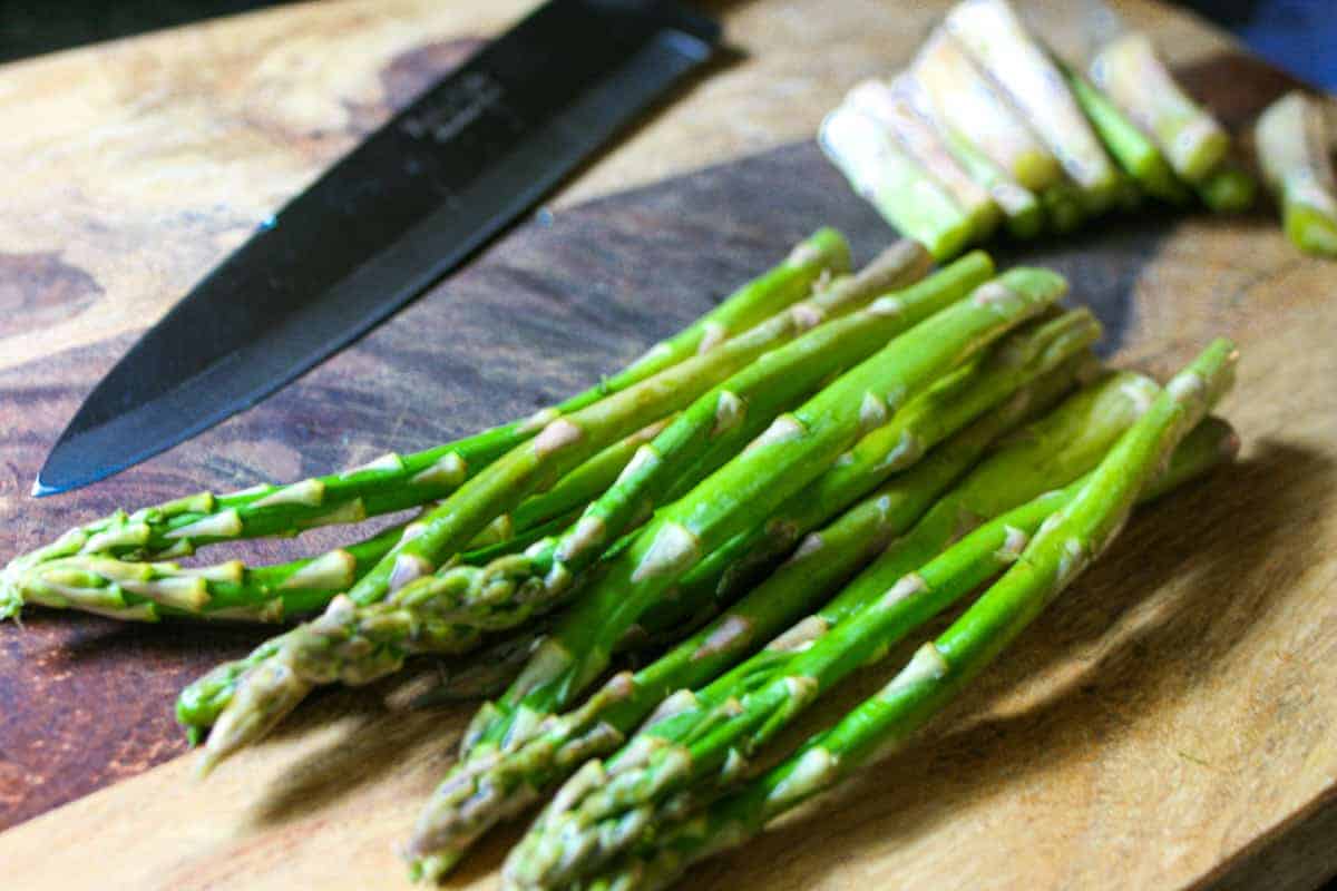 Trimmed bunch of raw asparagus on a cutting board with a butcher knife.