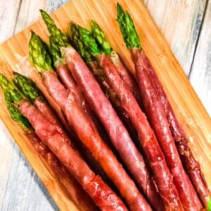 Prosciutto wrapped asparagus stacked on a cutting board.