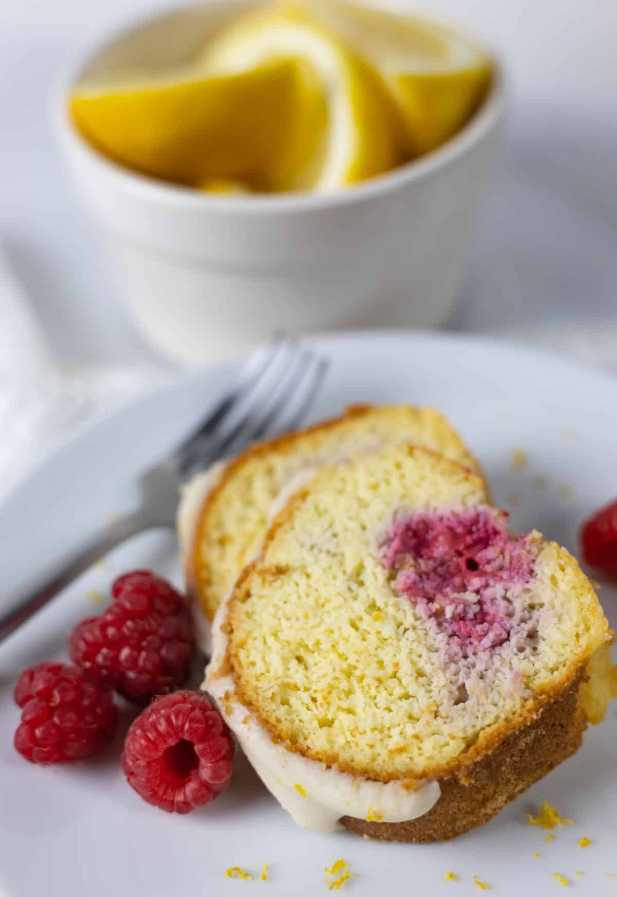 Two slices of raspberry lemon bundt cake on a plate with three raspberries and lemon zest.