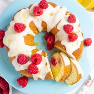 Lemon raspberry bundt cake topped with sugar-free icing on a blue cake pedestal with slices.