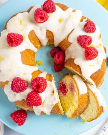 Lemon raspberry bundt cake topped with sugar-free icing on a blue cake pedestal with slices.