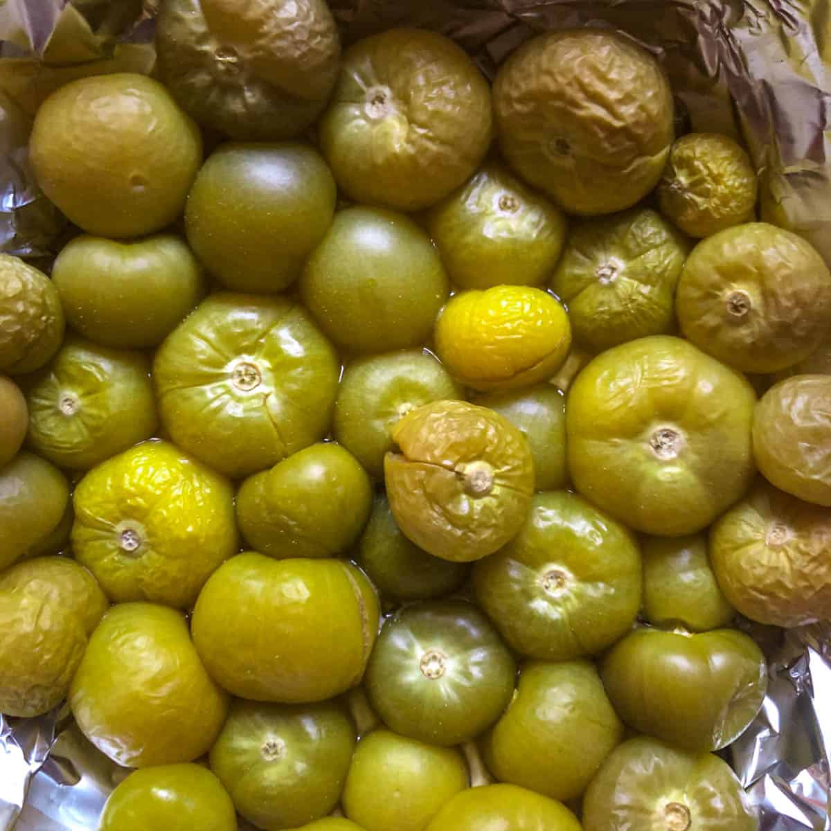 Smoked green tomatillos in foil on a baking sheet.