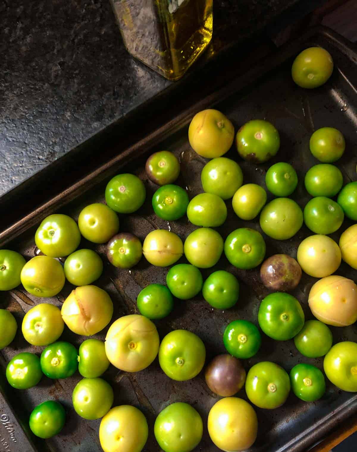 Raw, peeled green tomatillos on a baking sheet drizzled with olive oil.